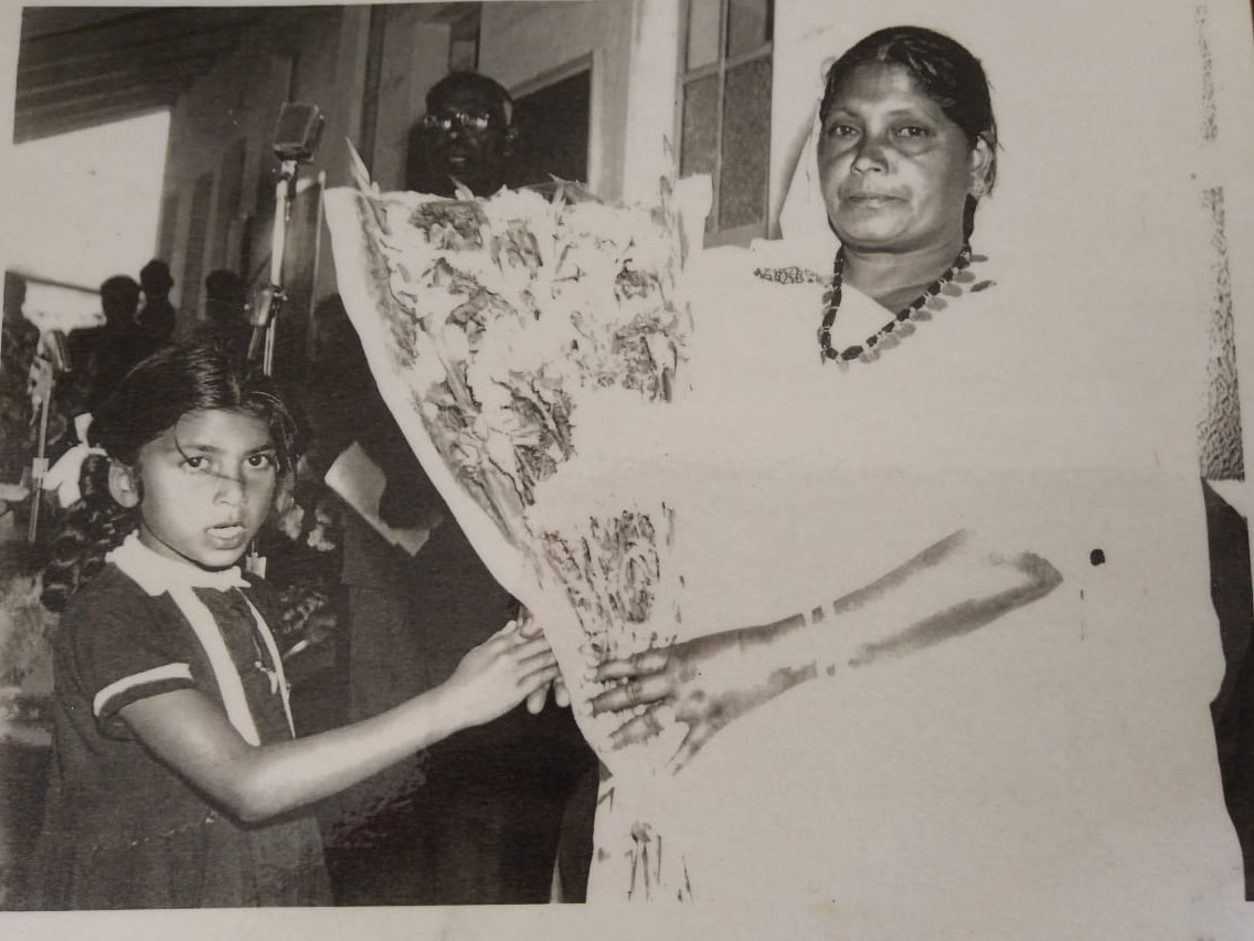 A black and white photograph of a woman and a schoolgirl together holding up a large decorated sheet of artwork